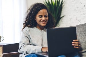 A young African American woman sitting in a chair smiles at something on her laptop as she types. This excitement could represent the goal of online EMDR therapy in Florida. An EMDR therapist in Tampa, FL can help you overcome past trauma with online EMDR in Florida. Contact us today!