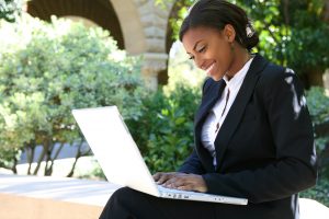 A businesswoman smiles as she types on her laptop on a stone bench. The represents the flexibility of online therapy in Florida. Contact an online therapist for support with online EMDR, online EMDR therapy, and other services.