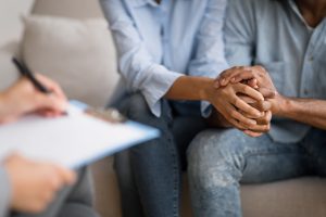 A couple join hands as they listen to a therapist holding a clipboard and pen. This represents couples therapy in Tampa, FL. Contact a couples therapist in Saint Petersburg, FL for more info today. 33609 | 33704 | 33703