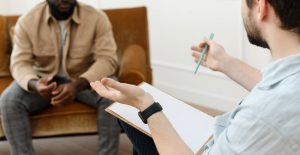 A person with a pen and clipboard gestures while sitting across from a man. Learn more about how dialectical behavior therapy in St. Pete, FL can offer support by contacting a DBT therapist in Tampa, FL today.