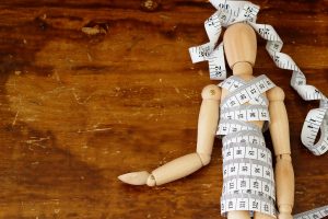 A wooden puppet model is surrounded by a measuring tape, representing the body image stress eating disorder treatment in Tampa, FL can help you overcome. Learn more about online eating disorder therapy in Tampa, FL by contacting an online eating disorder therapist in Tampa, FL today. 