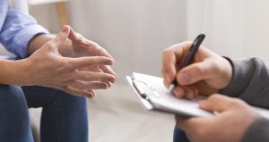 A close up of a person writing on a clipboard while sitting across from a person gesturing with their hands. This could represent a meeting with a therapist in St. Pete, FL. Learn more about the support a St. Pete therapist can offer by searching for “therapy tampa, fl” today.