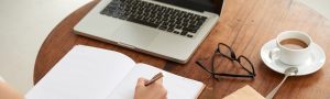 a woman writing in her journal in front of her laptop with a coffee sitting next to her, anxiety and behavioral health services, anxiety therapy 