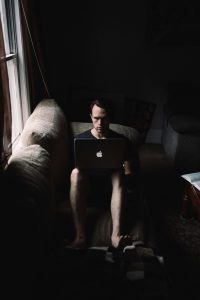 a man sitting in the dark on a couch with his laptop on his knees struggling with addiction, addiction therapy in tampa, substance abuse counseling