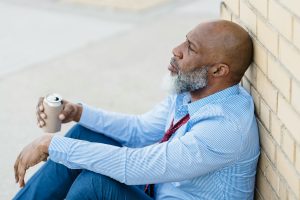 a black man with a beard leaning against a wall in dress suit and holding a beer, substance abuse, addiction therapy st petersburg fl