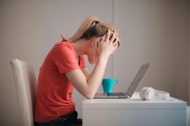 a young woman sitting at her laptop with her head in her hands, worrying, uncertain and anxious in St. Pete, Tampa Bay, FL