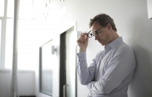 a middle aged man standing against a wall while at work with his glasses coming off of his face, ocd obsessive compulsive disorder, ocd therapy